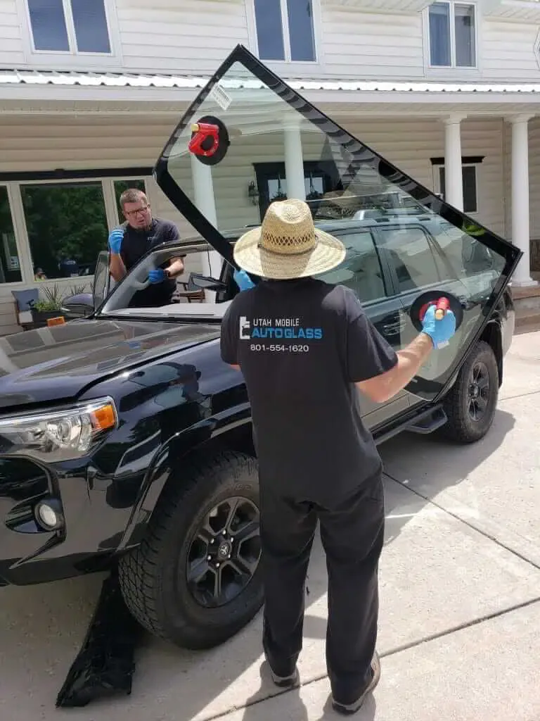 A man cleaning the windshield of a black SUV parked on a street.