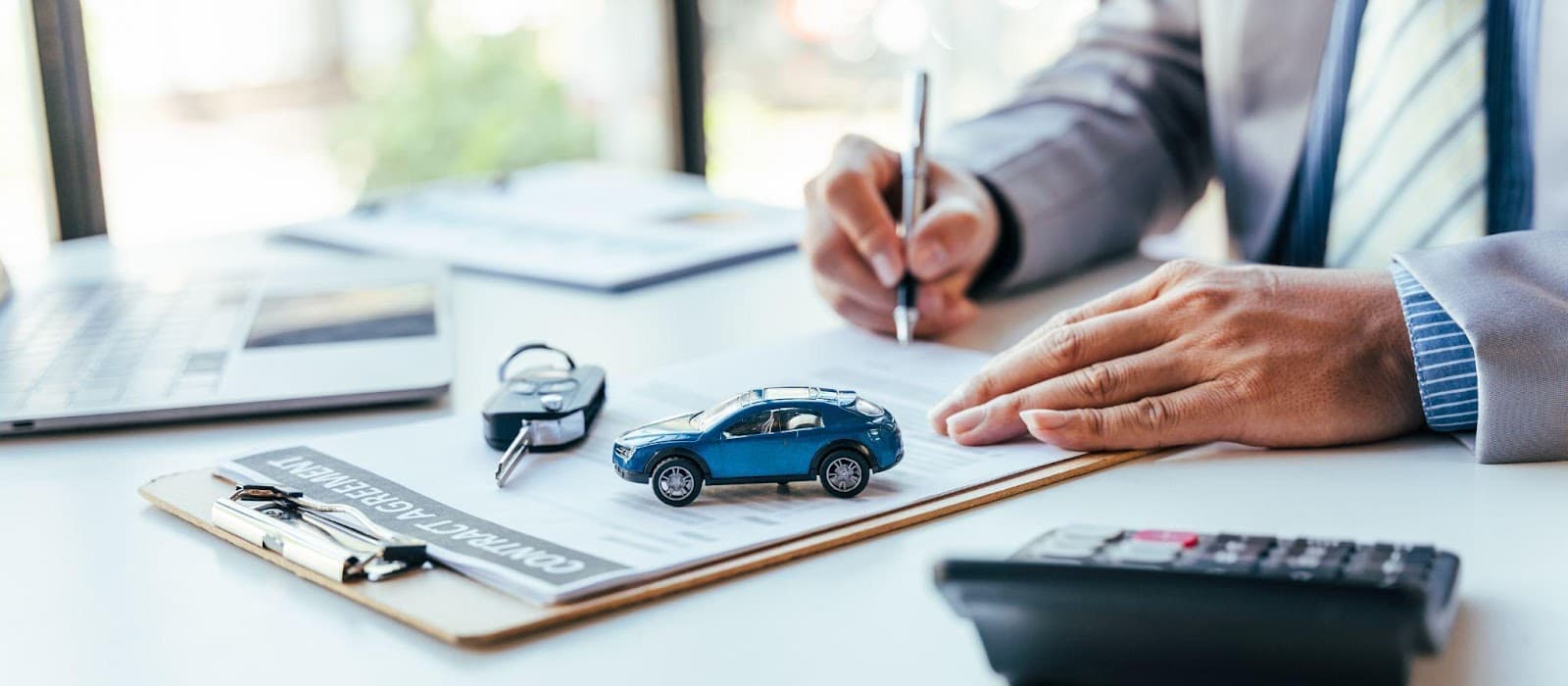 A man in a suit signing a contract with a car on a desk