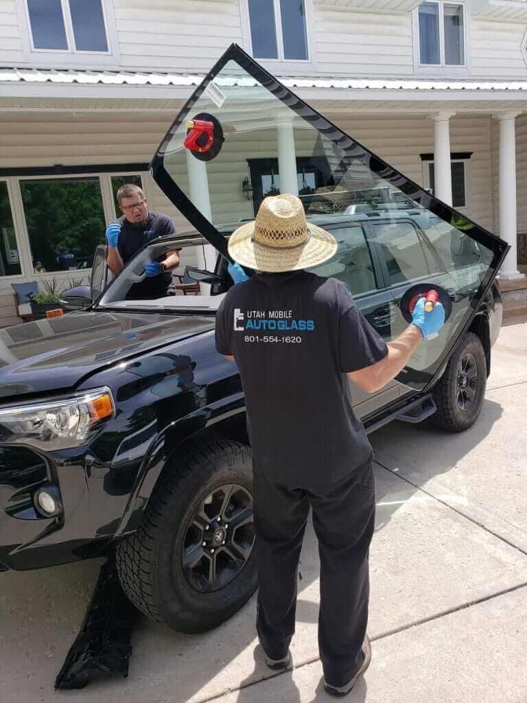 A man cleaning the windshield of a black SUV parked on a street.